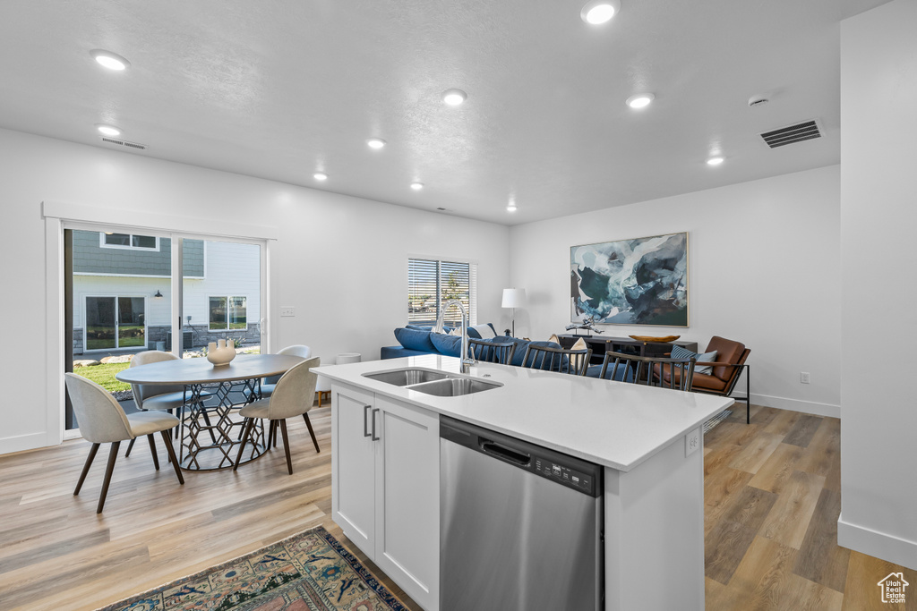 Kitchen with a kitchen island with sink, sink, stainless steel dishwasher, white cabinetry, and light hardwood / wood-style floors