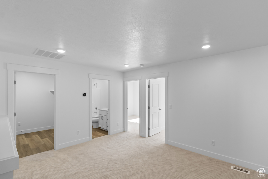 Unfurnished bedroom with a closet, ensuite bathroom, light carpet, and a walk in closet