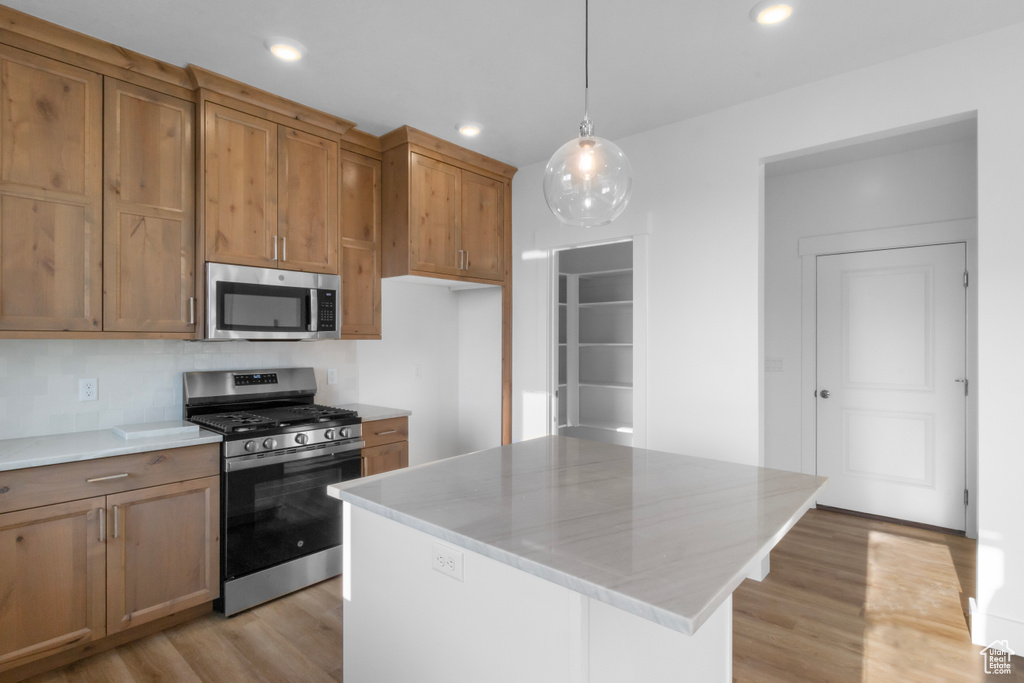 Kitchen with a kitchen island, hanging light fixtures, stainless steel appliances, and light wood-type flooring