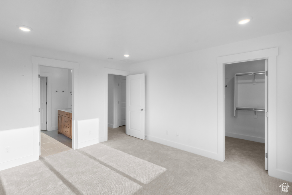 Unfurnished bedroom with a closet, a walk in closet, ensuite bath, and light colored carpet