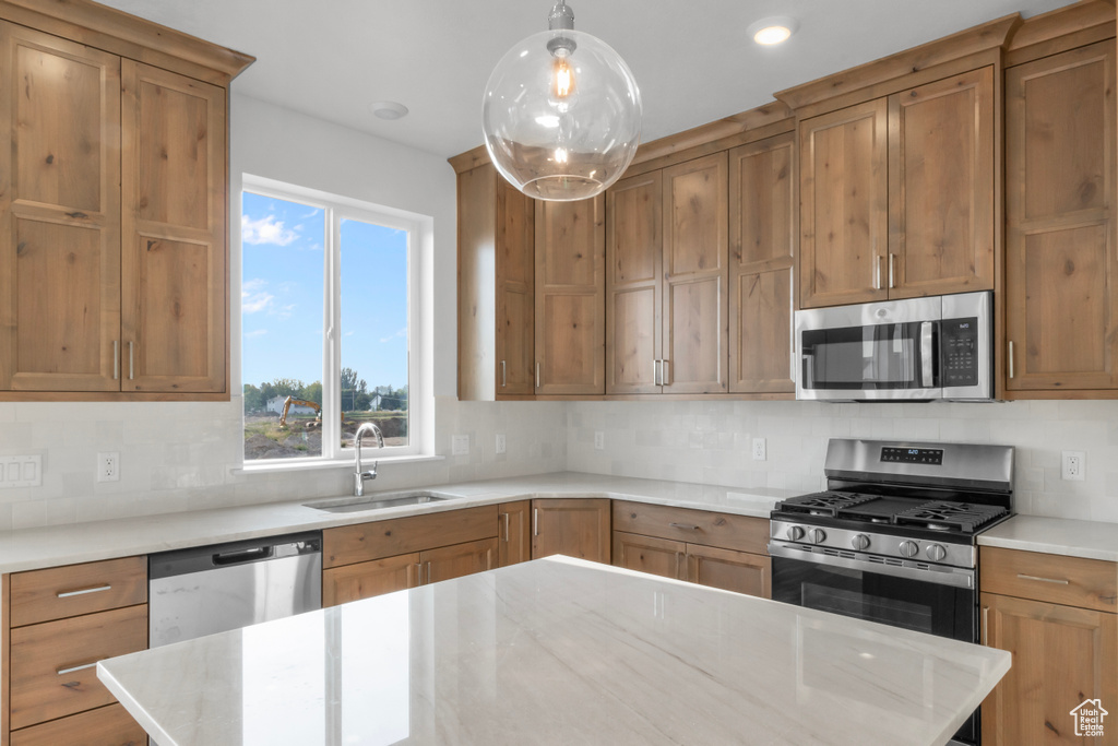 Kitchen featuring light stone countertops, appliances with stainless steel finishes, sink, pendant lighting, and decorative backsplash