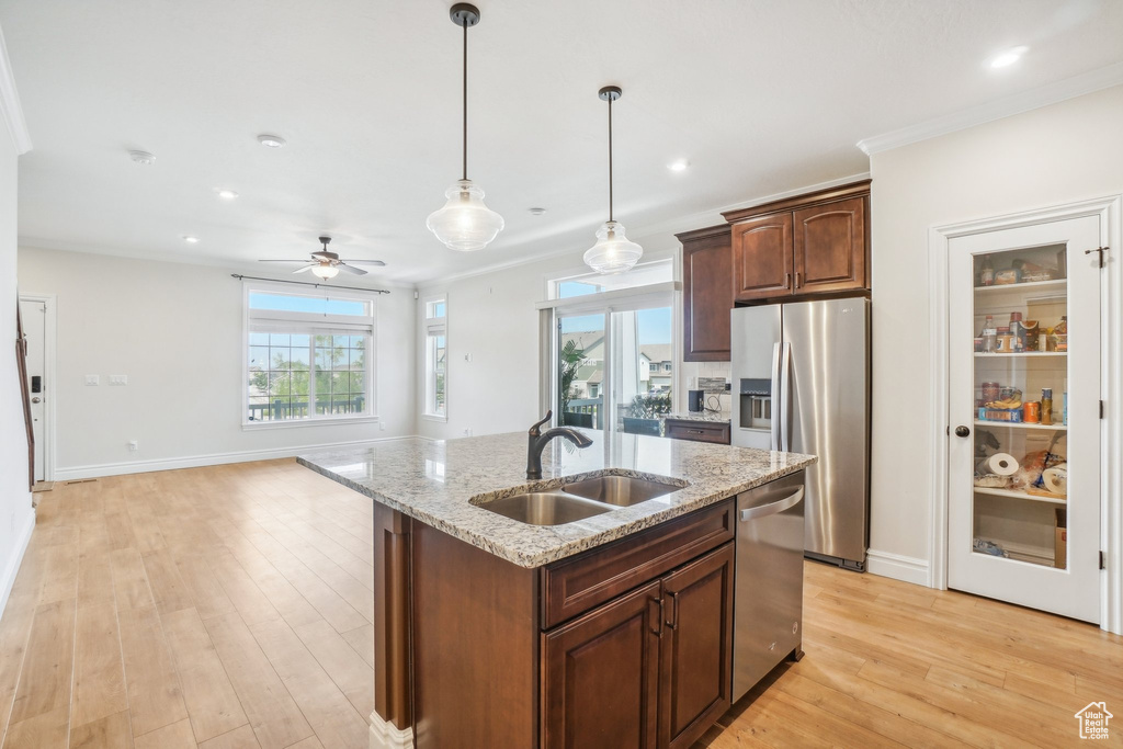 Kitchen with light stone countertops, sink, appliances with stainless steel finishes, and light hardwood / wood-style floors