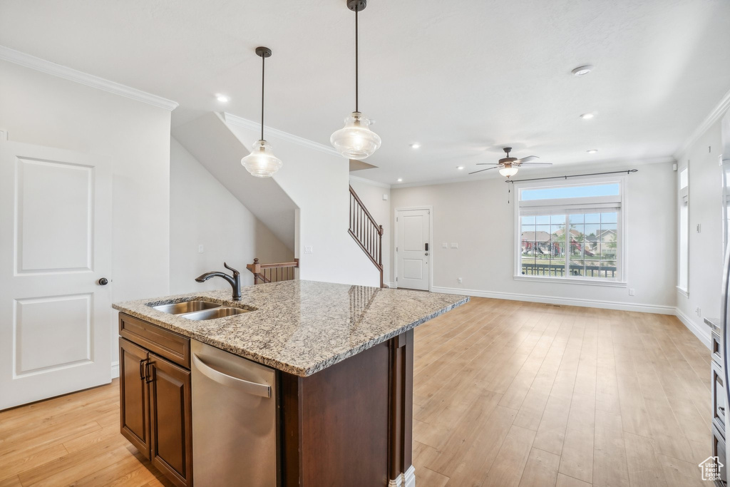 Kitchen featuring sink, light wood-type flooring, a center island with sink, and hanging light fixtures