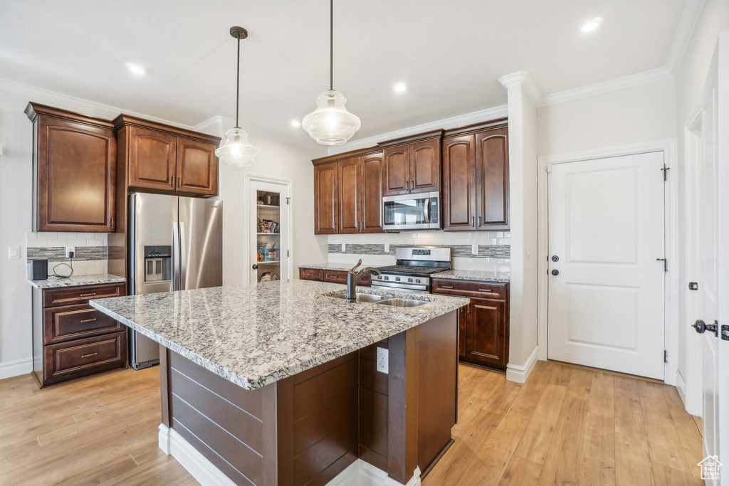 Kitchen featuring tasteful backsplash, a center island with sink, light stone counters, light hardwood / wood-style floors, and stainless steel appliances