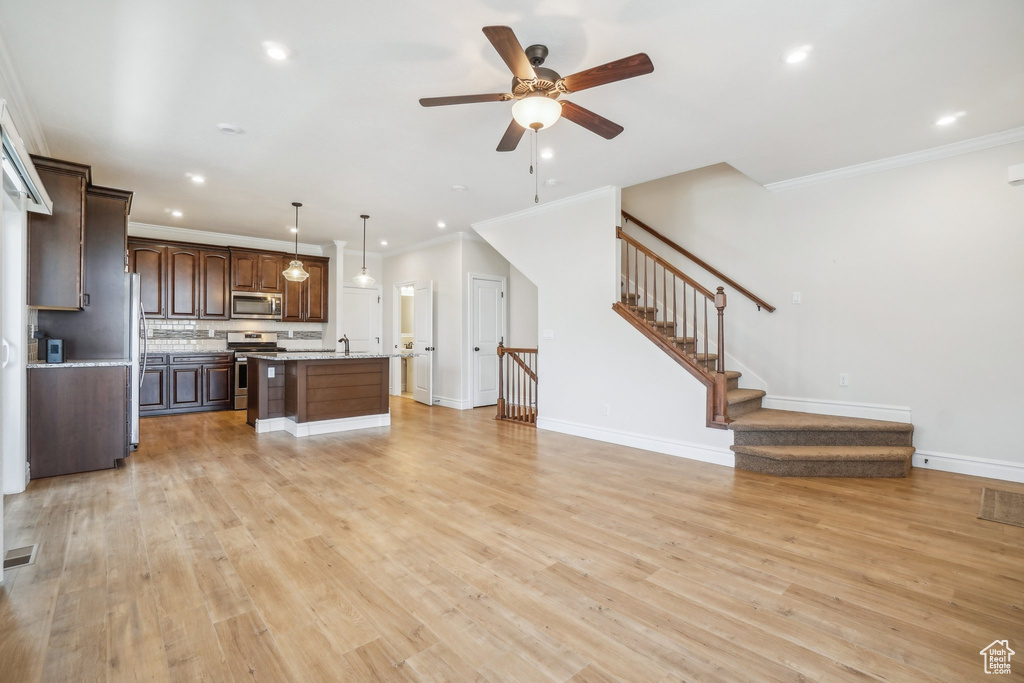 Kitchen featuring light hardwood / wood-style flooring, hanging light fixtures, stainless steel appliances, a center island with sink, and dark brown cabinetry