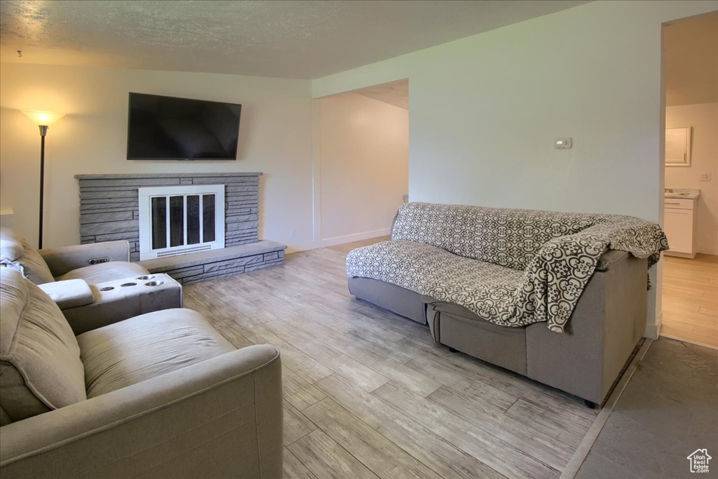 Living room with a stone fireplace, a textured ceiling, and light hardwood / wood-style flooring