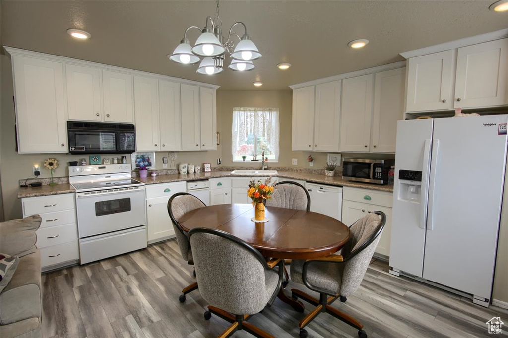 Kitchen featuring light hardwood / wood-style floors, sink, decorative light fixtures, white cabinetry, and white appliances