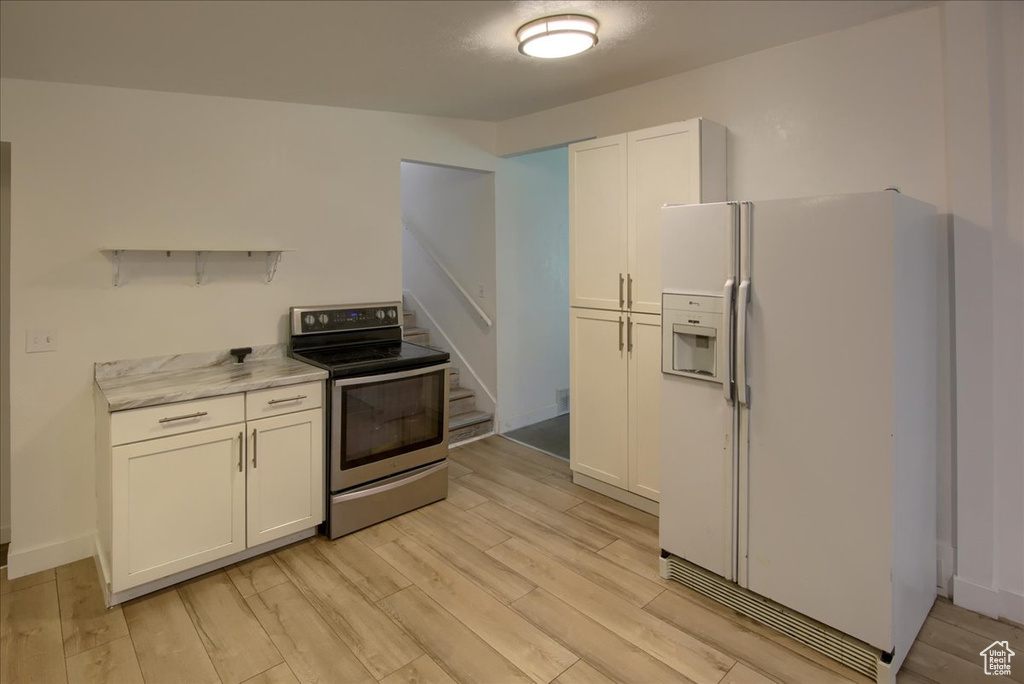 Kitchen with white cabinets, white fridge with ice dispenser, light stone countertops, stainless steel electric range oven, and light wood-type flooring