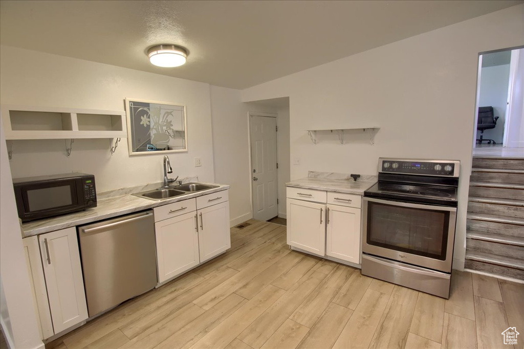 Kitchen with white cabinetry, light hardwood / wood-style flooring, appliances with stainless steel finishes, and sink