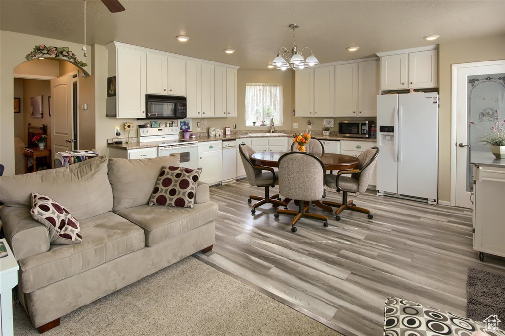 Kitchen with white appliances, light hardwood / wood-style floors, white cabinetry, and decorative light fixtures