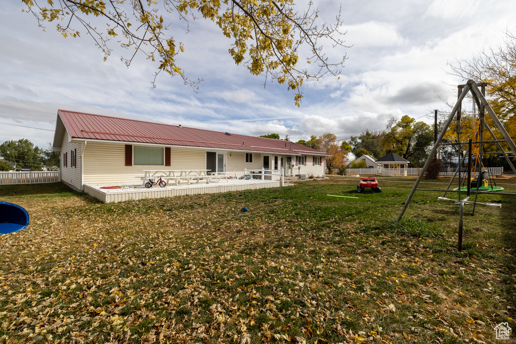 Rear view of property featuring a playground, a wooden deck, and a lawn