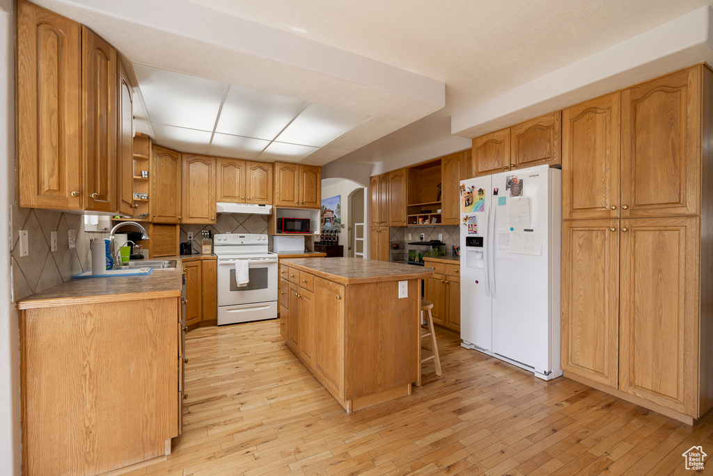 Kitchen featuring white appliances, sink, light wood-type flooring, a kitchen island, and backsplash