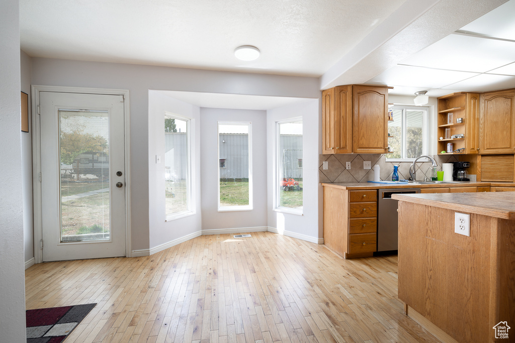 Kitchen with light hardwood / wood-style flooring, tasteful backsplash, dishwasher, and a wealth of natural light