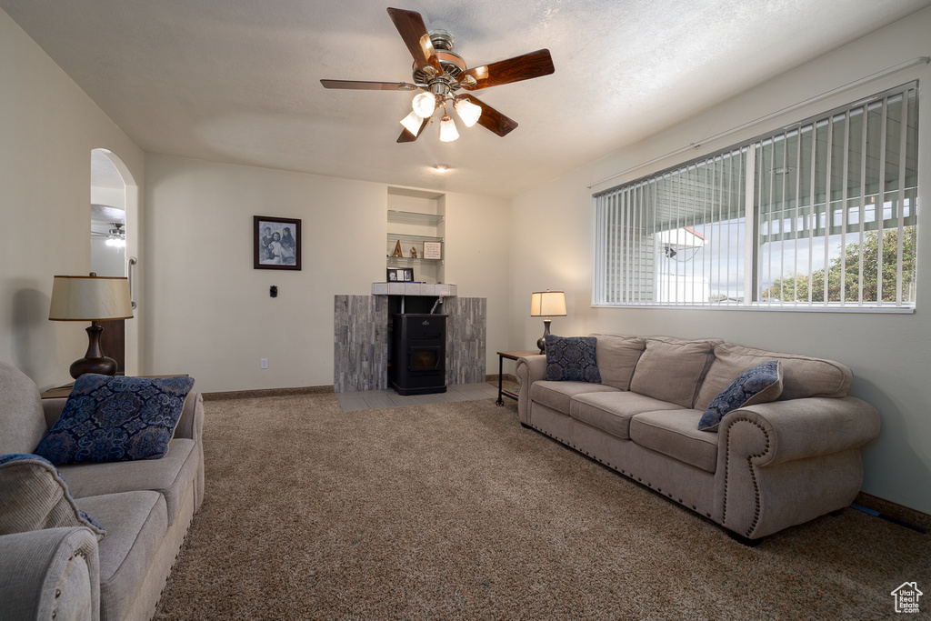 Living room with ceiling fan, a wood stove, and light colored carpet