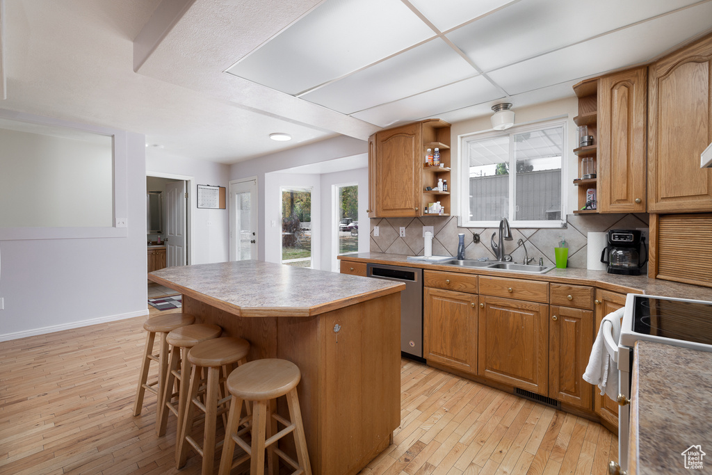 Kitchen featuring stainless steel dishwasher, sink, a kitchen island, and light wood-type flooring