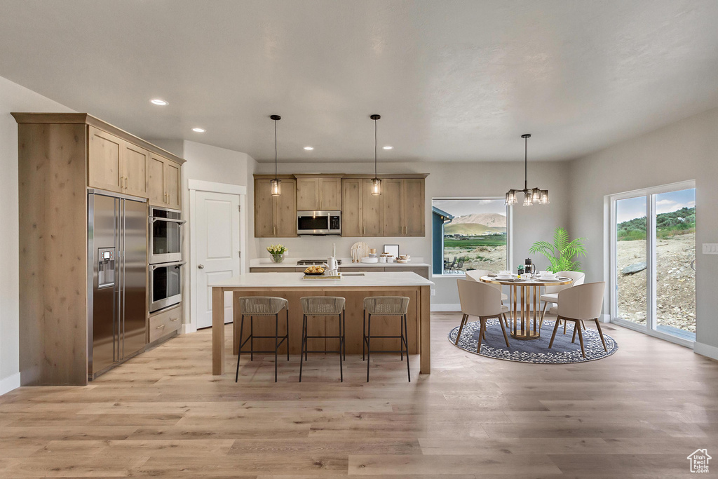 Kitchen featuring an island with sink, an inviting chandelier, stainless steel appliances, light hardwood / wood-style floors, and decorative light fixtures