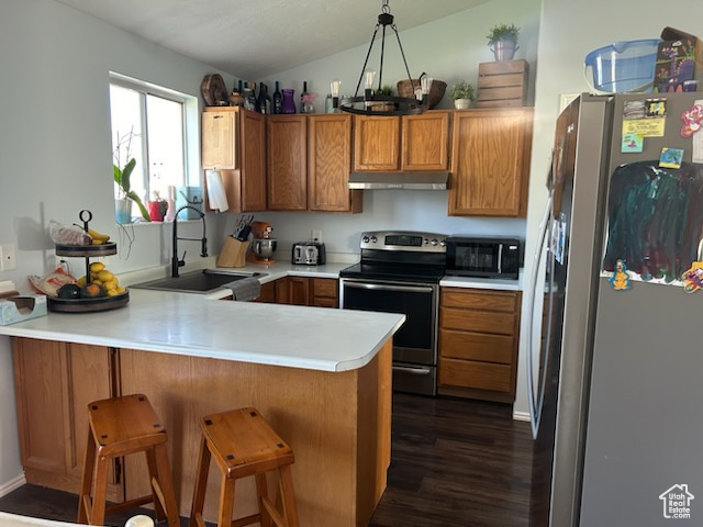 Kitchen featuring appliances with stainless steel finishes, sink, kitchen peninsula, decorative light fixtures, and dark wood-type flooring