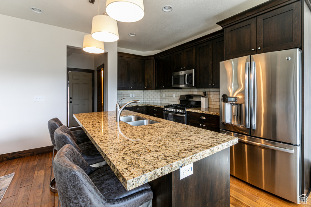 Kitchen with a center island with sink, sink, stainless steel appliances, and hardwood / wood-style flooring