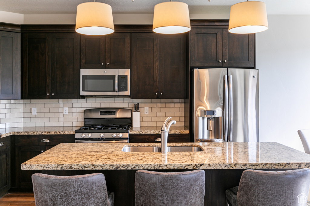 Kitchen with light stone countertops, sink, hanging light fixtures, stainless steel appliances, and dark hardwood / wood-style floors