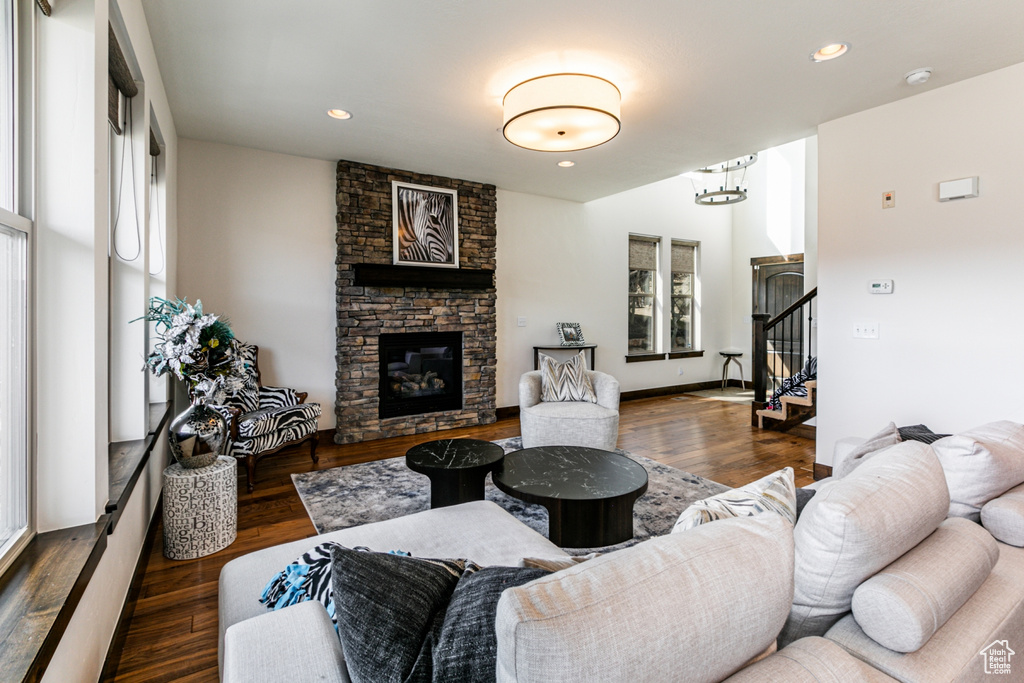 Living room featuring dark wood-type flooring, a stone fireplace, and a healthy amount of sunlight