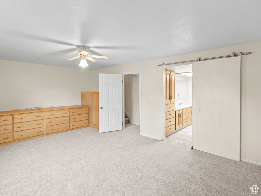 Unfurnished bedroom featuring a barn door, light colored carpet, connected bathroom, and ceiling fan