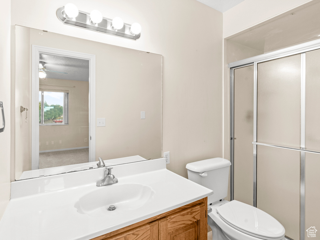 Bathroom featuring toilet, a shower with shower door, vanity, and ceiling fan