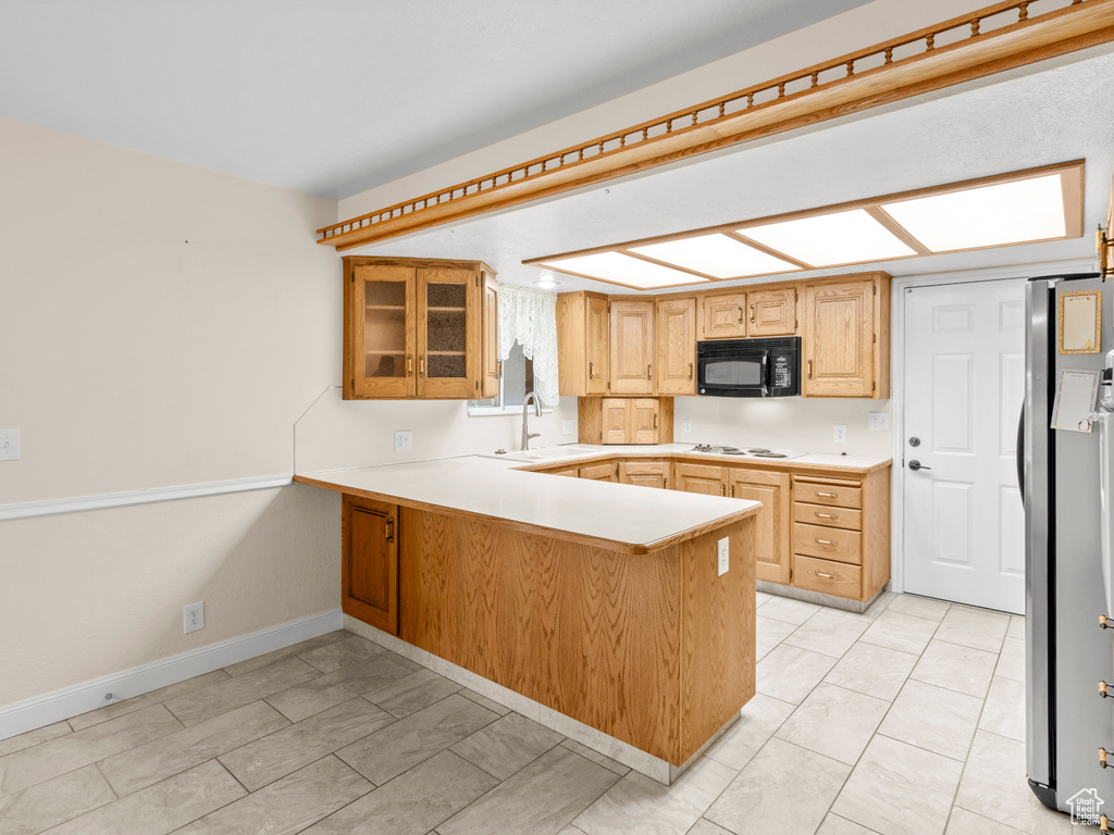 Kitchen featuring light tile patterned flooring, sink, kitchen peninsula, white cooktop, and stainless steel refrigerator