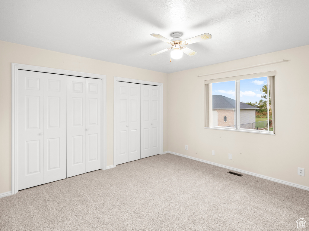 Unfurnished bedroom with ceiling fan, a textured ceiling, multiple closets, and carpet floors