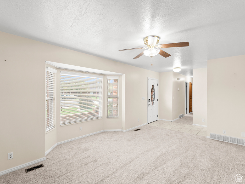 Empty room with light carpet, a textured ceiling, and ceiling fan