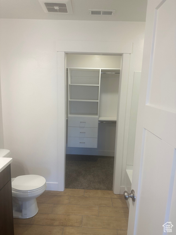 Bathroom with vanity, hardwood / wood-style floors, toilet, and a tub to relax in