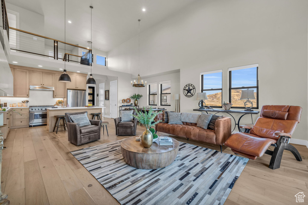 Living room with a chandelier, light wood-type flooring, and high vaulted ceiling