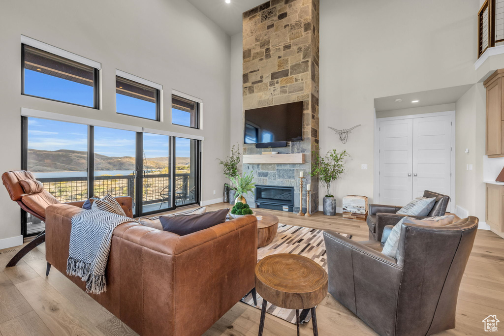 Living room with a towering ceiling, a stone fireplace, and light wood-type flooring