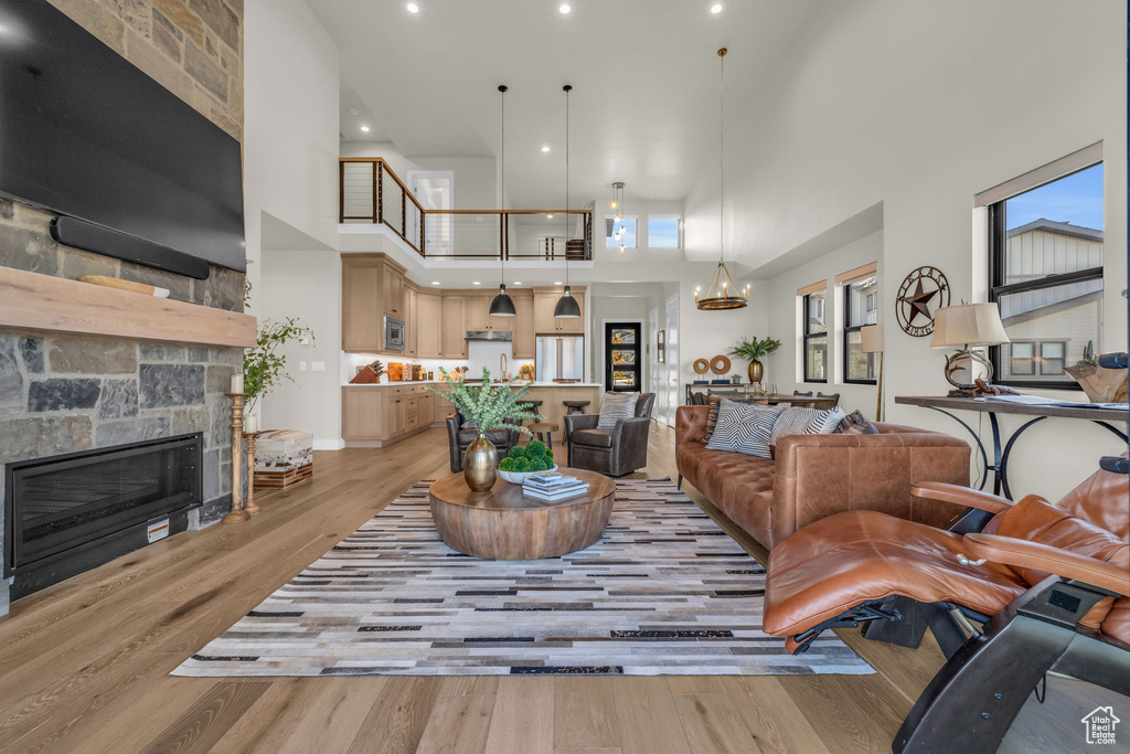 Living room with a towering ceiling, light hardwood / wood-style flooring, a chandelier, and a stone fireplace