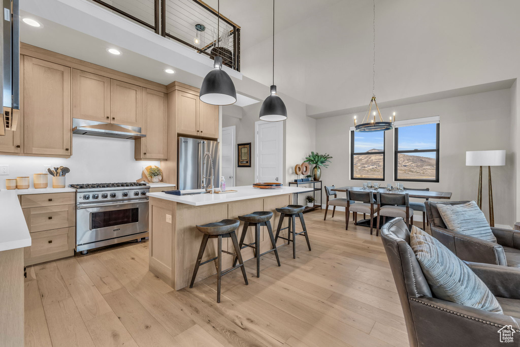 Kitchen featuring light brown cabinets, high quality appliances, decorative light fixtures, and light wood-type flooring