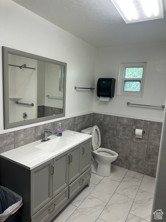 Bathroom featuring vanity, toilet, tile walls, and a textured ceiling