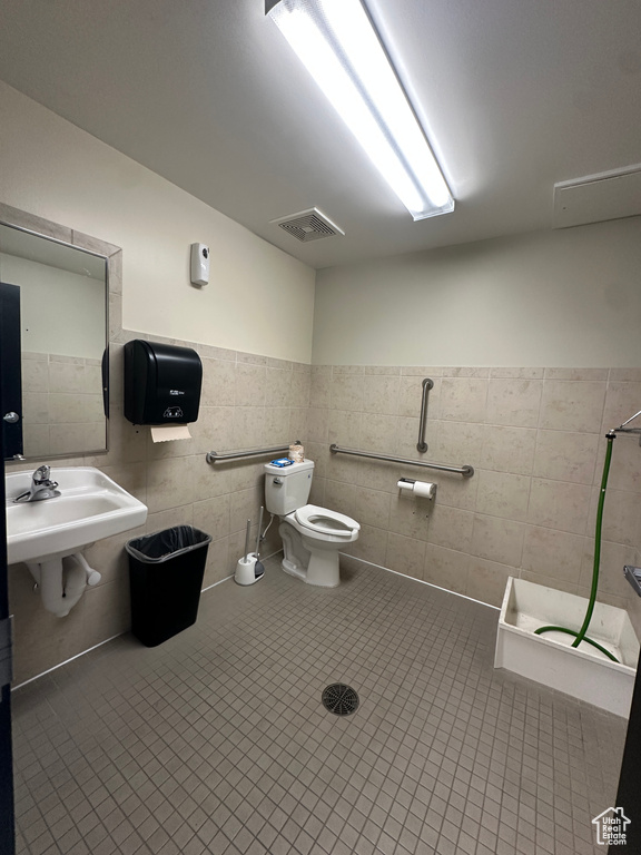 Bathroom featuring a shower, tile walls, toilet, sink, and tile patterned flooring