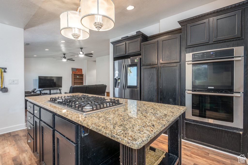 Kitchen with dark brown cabinets, a center island, stainless steel appliances, light stone counters, and light hardwood / wood-style flooring