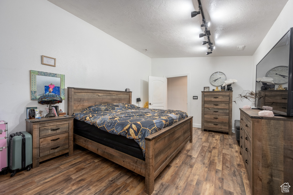 Bedroom featuring a textured ceiling, track lighting, and dark hardwood / wood-style flooring