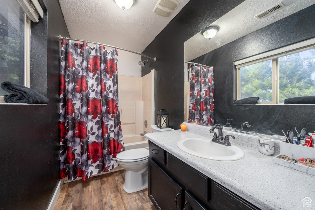 Full bathroom featuring hardwood / wood-style floors, shower / tub combo, a textured ceiling, toilet, and vanity