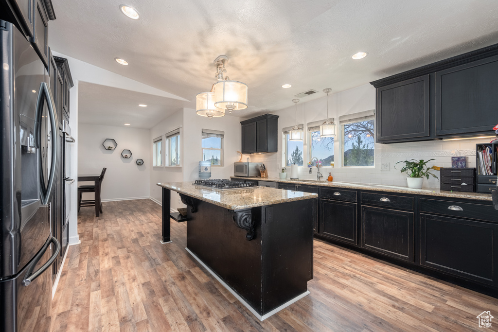 Kitchen with a kitchen island, a breakfast bar area, stainless steel appliances, decorative light fixtures, and light wood-type flooring