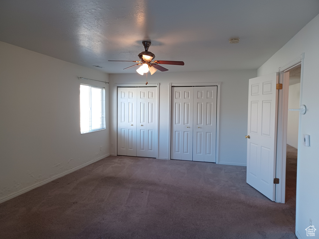 Unfurnished bedroom with dark colored carpet, a textured ceiling, two closets, and ceiling fan