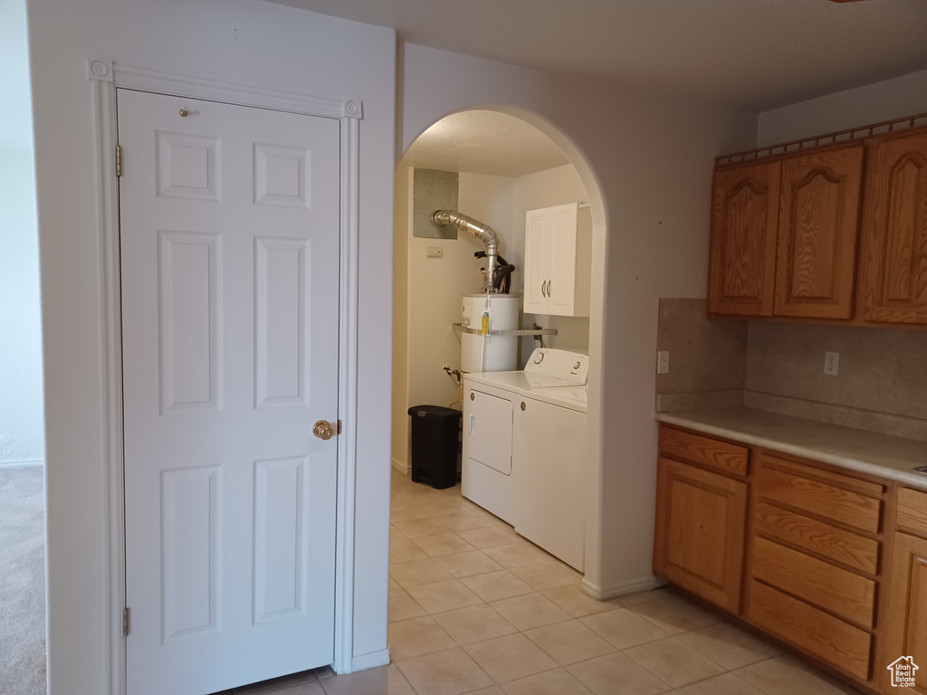 Laundry area with strapped water heater, independent washer and dryer, light tile patterned floors, and cabinets