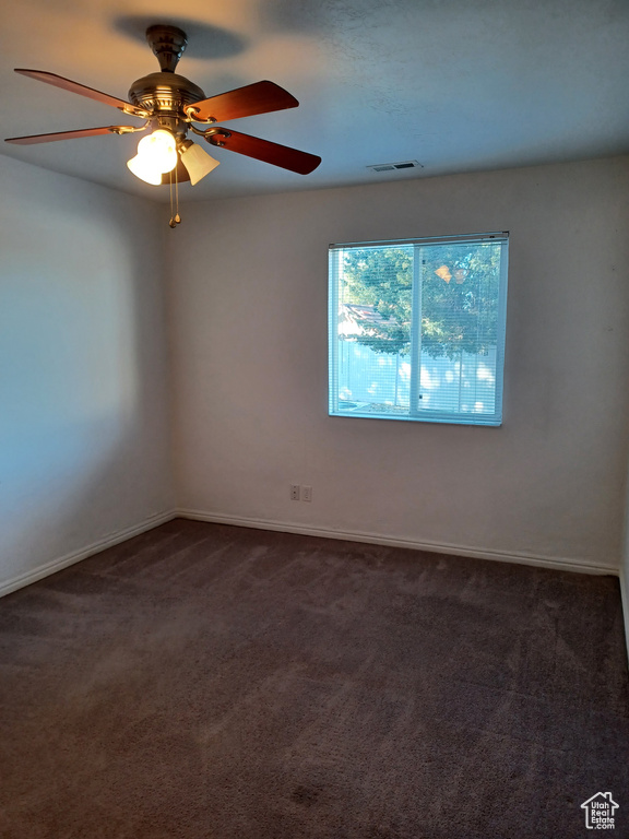 Spare room with ceiling fan and dark colored carpet