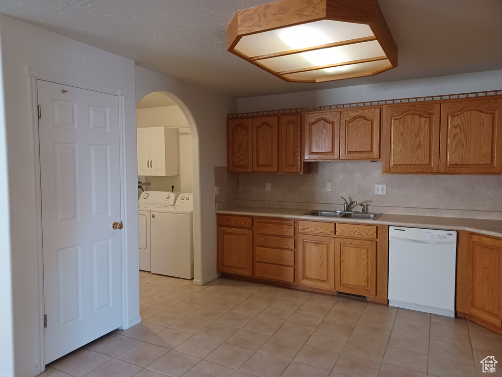 Kitchen featuring light tile patterned floors, white dishwasher, sink, and washing machine and clothes dryer