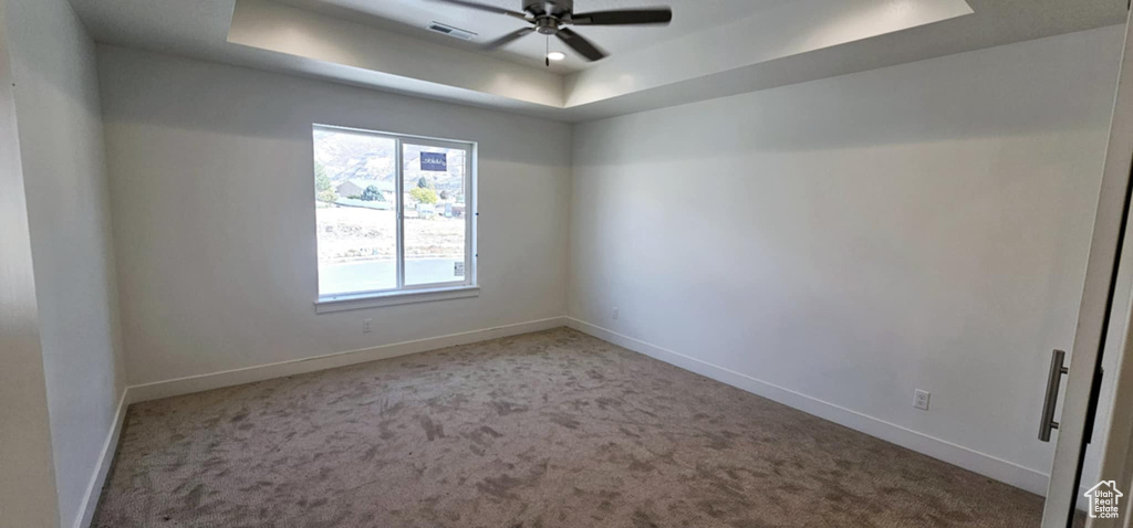 Carpeted empty room with ceiling fan and a raised ceiling