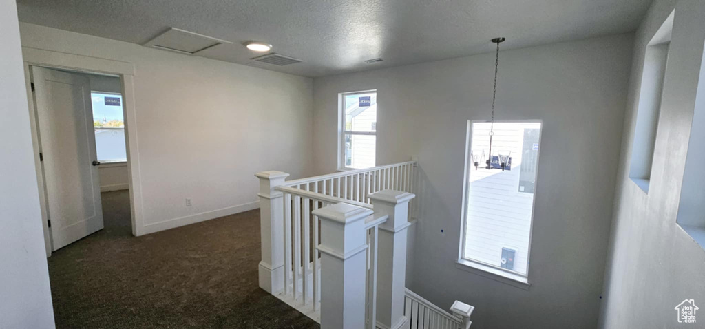 Hallway with a textured ceiling and dark carpet