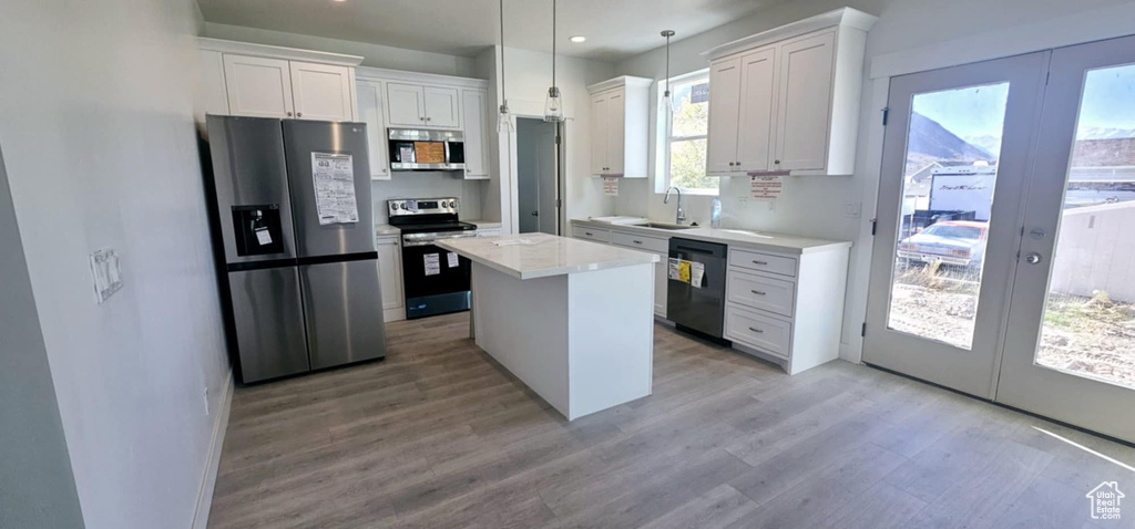 Kitchen with appliances with stainless steel finishes, a center island, decorative light fixtures, and white cabinets