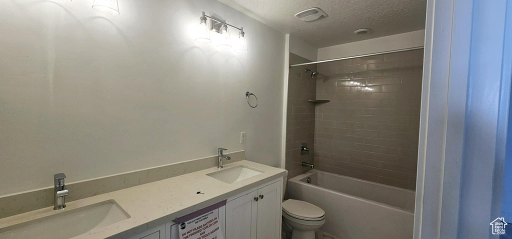 Full bathroom with vanity, tiled shower / bath combo, a textured ceiling, and toilet