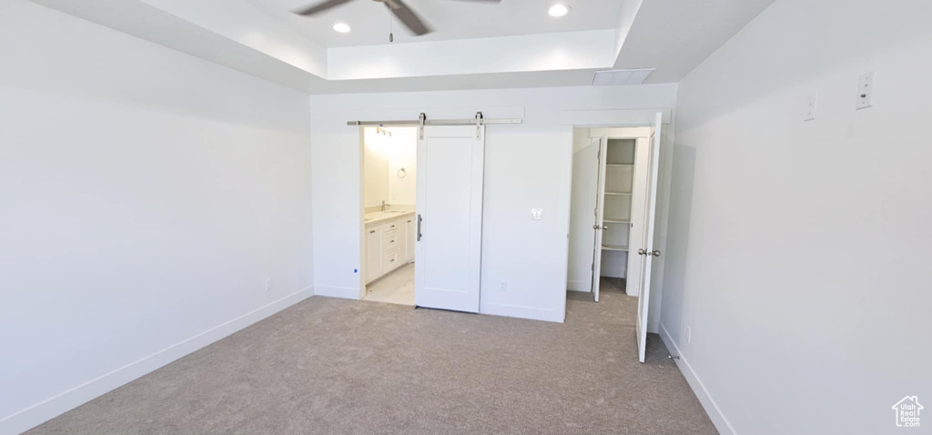 Unfurnished bedroom featuring ensuite bathroom, a barn door, light colored carpet, and ceiling fan