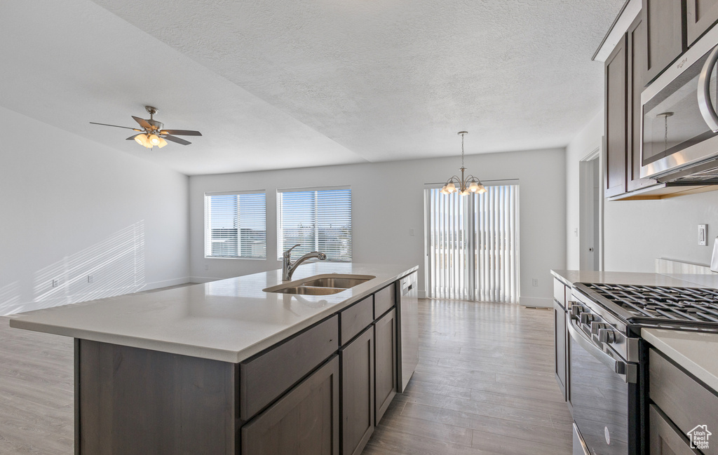 Kitchen with appliances with stainless steel finishes, light hardwood / wood-style floors, ceiling fan with notable chandelier, a center island with sink, and sink